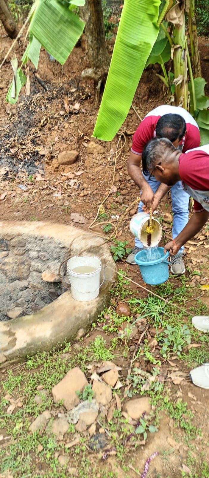 Two men collecting and pouring water near a well source