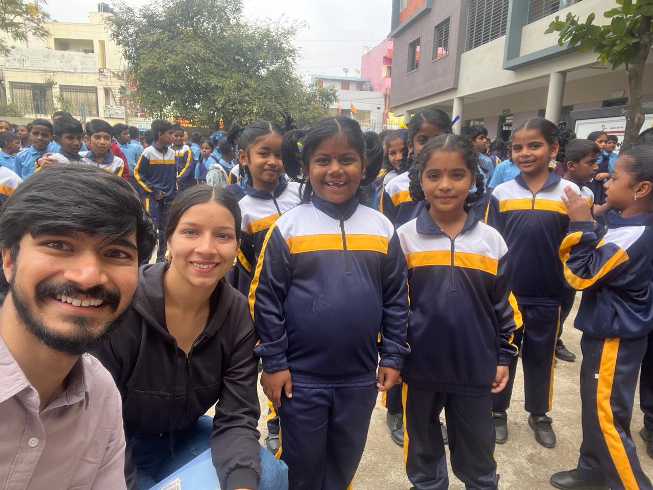 Smiling school children in uniforms posing with young volunteers outside.