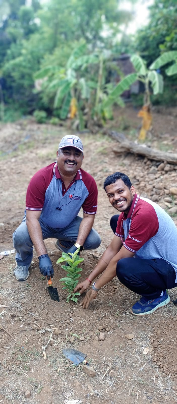 Two men smiling while planting a sapling during community drive
